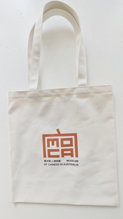 Reverse of a natural-coloured tote bag with a compact red and dark brown bilingual MOCA logo.